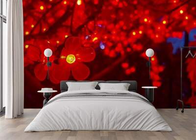 red christmas sakura flowers with petals in the form of bright light bulbs on a tree on a dark background framed by leaves in bushes festive background Wall mural