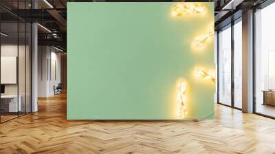 Christmas lights on light green background, flat lay with holiday garland Wall mural