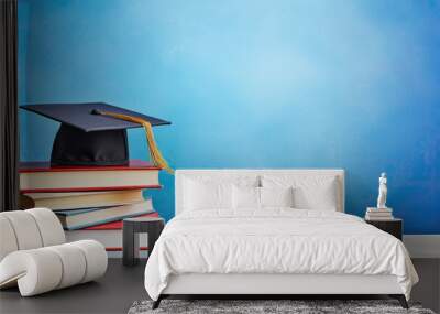 School books and graduation hat on table with blue wall background Wall mural