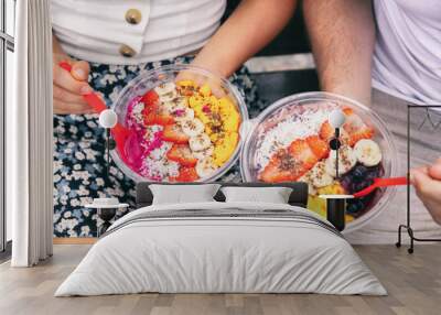 Acai bowl and pitaya dragonfruit smoothie healthy breakfast bowls young friends eating together. Couple man and woman eating sitting outside in park for lunch break. Closeup on food. Wall mural