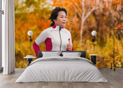 Active woman running and jogging. Middle aged Asian mature female jogger outdoor living healthy lifestyle in beautiful autumn city park in colorful fall foliage. Asian Chinese lady in her fifties. Wall mural