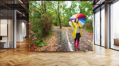 Asian Autumn woman happy after rain walking with umbrella. Female model looking up at clearing sky joyful on rainy fall day wearing yellow raincoat outside in nature forest. Multiracial Asian girl. Wall mural