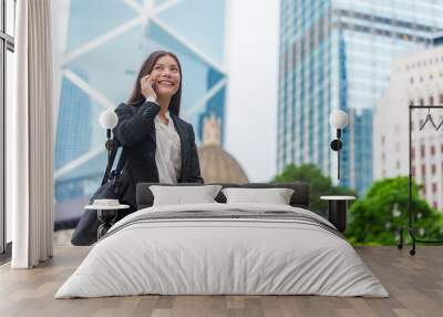 Asian businesswoman talking on mobile phone walking in Hong Kong city street to office, skyscrapers cityscape background. Young woman on smartphone happy. Multiracial Chinese Caucasian lady. Wall mural