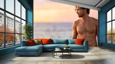 Beach body fit handsome man with six pack abs shirtless on summer Hawaii vacation sunset. Surfer lifestyle. Wall mural