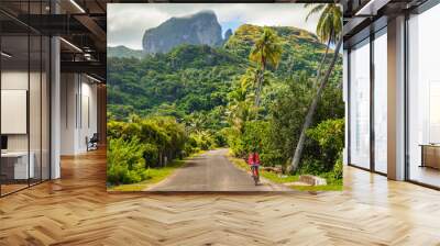 Biking tourist on summer vacation travel discovering by e-bike cycling through forest of Bora Bora island in Tahiti, French Polynesia. Wall mural