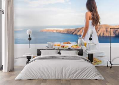 Breakfast table and luxury travel woman on santorini. Well balanced perfect breakfast table served at resort. Female tourist is looking at beautiful view of sea and caldera enjoying her vacation. Wall mural