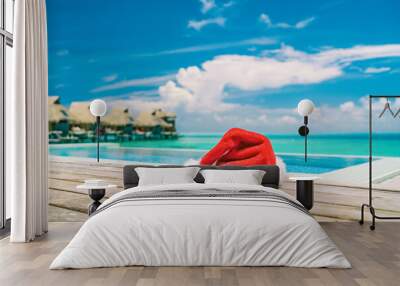 Christmas Santa Claus hat by the swimming pool at luxury vacation resort for high end summer destination sun vacation getaway during winter holiday. Overwater bungalows villas. Wall mural