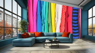 Closet women's fashion outfits clothes arranged in rainbow colors assorted. Clothing store dresses hanging on shopping rack. Variety of fabrics and patterns, wool, polyester, polka dots, stripes. Wall mural