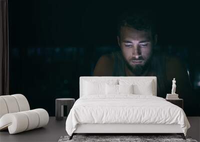 Dark night man looking at mobile phone screen texting late at night awake in bed insomnia or outside in city with skyline background. Serious looking guy depressed addicted to social media. Wall mural