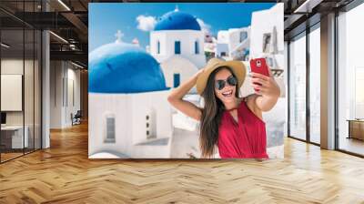 Europe luxury travel destination Santorini cruise tourist Asian woman having fun taking self portrait photo with mobile phone at famous three blue domes church in Oia, Greece. Wall mural