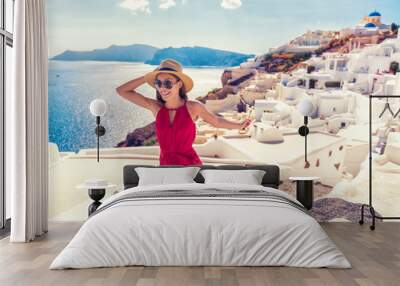 Europe travel fun - woman tourist running of joy in Santorini city luxury holiday destination. Cruise in Greece for summer holidays. Asian girl in red dress and hat with greek white houses background. Wall mural