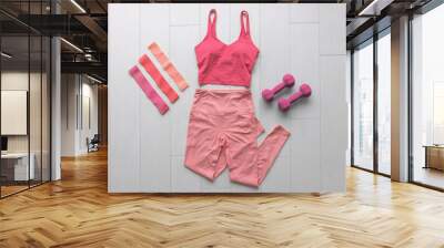 Fitness clothes flat lay workout at home with resistance bands and dumbbell weights. Pink athleisure fashion clothing top view on white wood floor. Wall mural