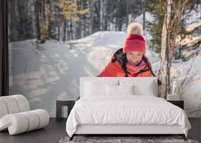 Happy Asian woman laughing walking in snow forest during winter. Beautiful portrait of young adult smiling wearing cold weather hat and gloves, orange jacket. Wall mural