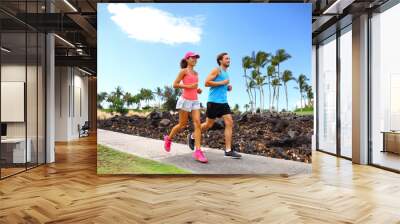 Happy couple of runner friends running training for marathon race together in summer jogging on street sidewalk neighborhood park. Wall mural