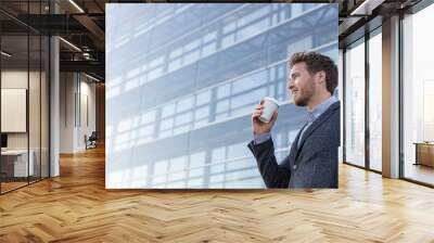 Happy young business professional man drinking coffee cup on his morning commute walk to work. Caucasian businessman with hot drink on office background looking away with satisfaction. Wall mural