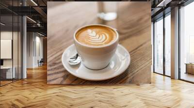 Latte art in cappuccino coffee cup at cafe table. Closeup of rosetta flower drawing in foam. Wall mural