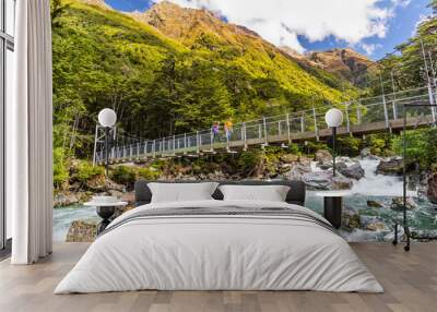 New Zealand tramping people crossing river bridge. Hikers couple backpackers walking hiking together with backpacks on Routeburn Track trail path. Wall mural