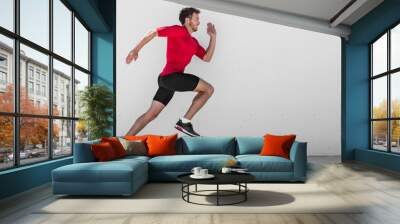 Running man runner training doing outdoor city run sprinting along wall background. Urban healthy active lifestyle. Male athlete doing sprint hiit high intensity interval training. Wall mural