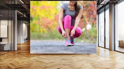 Running shoes woman runner tying shoe lace for run. Happy smiling girl getting ready for jogging lacing run shoe laces. Female sport fitness runner outdoors on forest path in autumn fall season. Wall mural