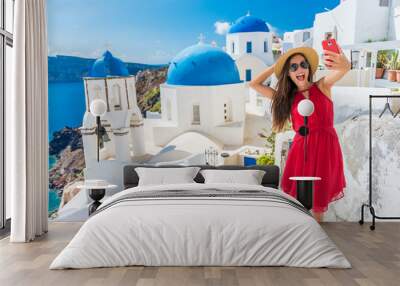 Santorini tourist girl on cruise holiday taking selfie photo with phone at famous three domes church, European tourism attraction in Greece. Asian woman on vacation. Wall mural