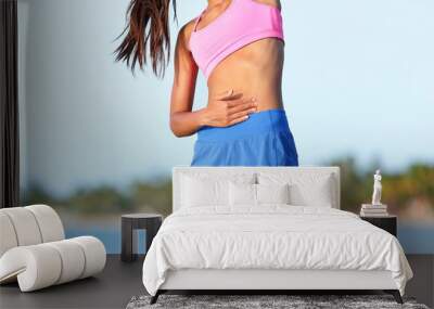 Side stitch stomach pain. Woman runner cramps. Jogging girl with stomach side pain during jogging work out. Female athlete on beach. Wall mural