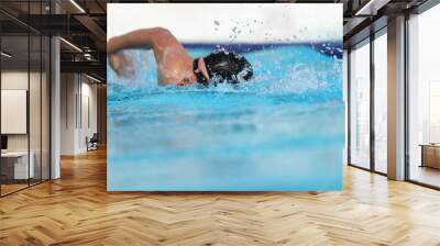 Swimming pool athlete training indoors for professional competition. Swimmer man on swim practice in stadium doing crawl with arm splashing water. Copy space on blue water background. Wall mural