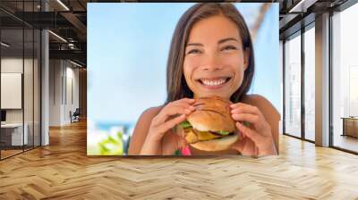 Woman eating fast food chicken burger at resort restaurant. Asian girl enjoying summer vacation at outdoor cafe with lunch meal, hamburger and fries. Wall mural