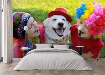 Small children dressed in elegant festive fun wigs with their dog and play with it in nature in the summer. Wall mural