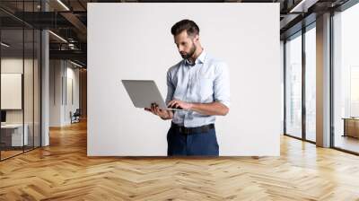 having some emails to look through. handsome young man using his laptop while standing against white Wall mural