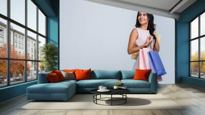 In love with shopping. Beautiful young woman holding shopping bags and looking away with smile while standing against white background Wall mural