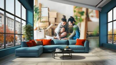 cheerful young family of man and woman wearing casual clothes makes project of decoration for new apartment on laptop sitting on floor near pile of boxes Wall mural