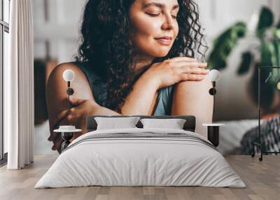 Curly haired overweight young woman in grey top and shorts with satisfaction on face accepts curvy body shape standing in stylish bedroom closeup Wall mural