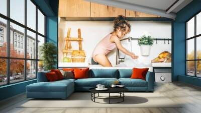 Funny happy baby girl playing in a kitchen sink. Wall mural