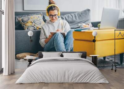 Student woman learning with headphones and laptop and taking notes at home. Wall mural