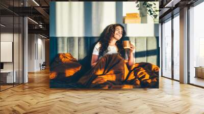 Woman drinking coffee in her bed at sunny morning. Wall mural