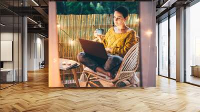 Woman using laptop at balcony of her apartment at the night. Wall mural