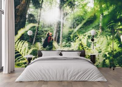 Woman with backpack walk through forest with fern leaves at the sunset. Traveling in nature concept. Girl enjoying the forest. Сoncept of nature and happy life, adventure. Wall mural