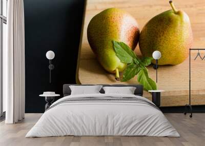 Two pears with fresh basil leaves on a wooden cutting board with black background Wall mural