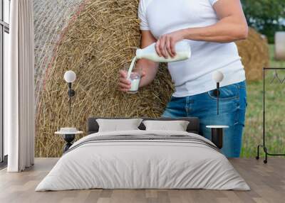 man pours fresh milk into a cup against the background of a field and hay Wall mural