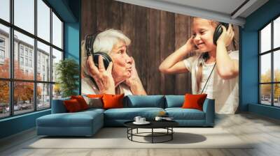 old woman and little girl in headphones listening to music grandmother and granddaughter Wall mural