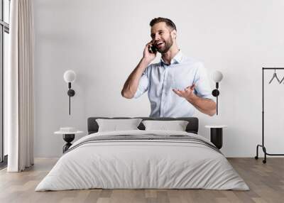 So glad to hear you! Handsome young man using his phone with smile while standing against white background. Wall mural