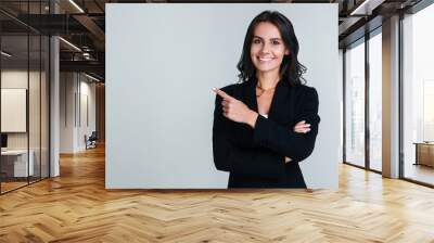 You need to look here! Beautiful young businesswoman pointing away and looking at camera with smile while standing against white background Wall mural