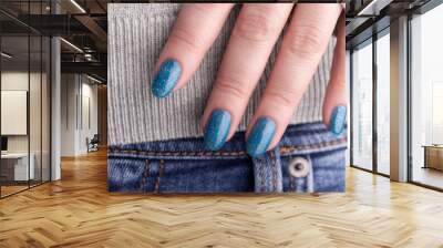 Female hand with beautiful manicure - blue glitter nails on jeans denim, closeup fingers. Nail care concept Wall mural