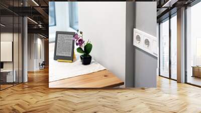 Group of white european electrical outlets and a switch located on a gray wall in a light modern kitchen with flower and e-book on the table by the window. Selective focus Wall mural