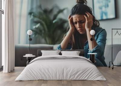 Unhappy young lady sitting on sofa, troubled by financial woes, holding head in hands. Wall mural