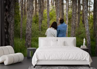 Young couple standing together in forest, with man pointing up. Man and woman looking at something interesting in the forest. Wall mural