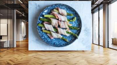 fresh asparagus wrapped in bacon in a blue plate on a light background Wall mural