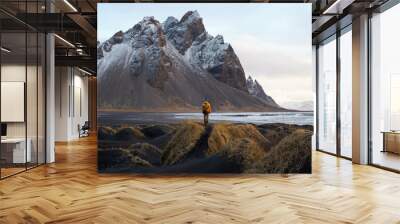 A tourist  stands on the beach, admiring the majestic reflection of the Vestrahorn mountain at Cape Stokksnes, Iceland, as the sun rises on the horizon. The beautiful snow-capped mountains. Wall mural