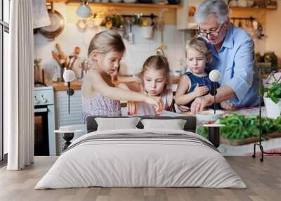 Kids and grandmother cooking italian pizza in cozy home kitchen for family dinner. Cute girls are preparing homemade food. Old senior woman is teaching three little sisters. Children chef concept. Wall mural