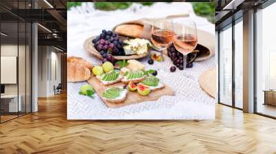 Romantic picnic with two wineglasses, delicious food, healthy fruits: avocado, grapes, figs. Straw hat, bag, sandwiches, croissants, cheese are on white plaid. Lunch in italian or french style Wall mural